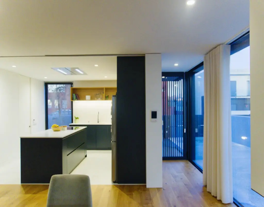 An open-plan kitchen leading into the dining area, with lighting provided by floor-to-ceiling windows.