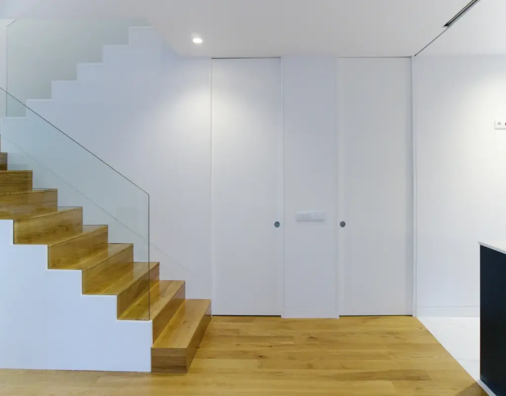 A wooden staircase leading to the upper floor, with a glass balustrade alongside floor-to-ceiling doors.