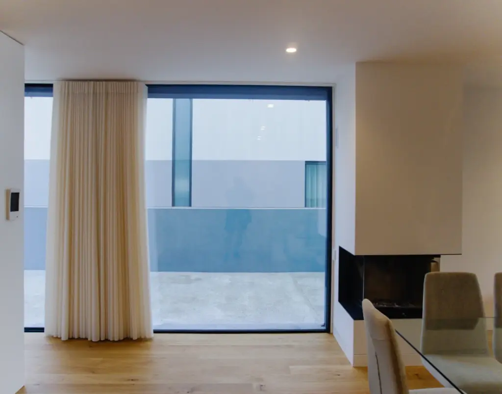 A window with curtains in the dining area, next to the fireplace near the table.