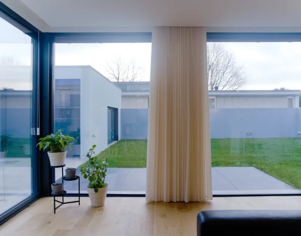 A window with white curtains in the living room, overlooking the lawn.